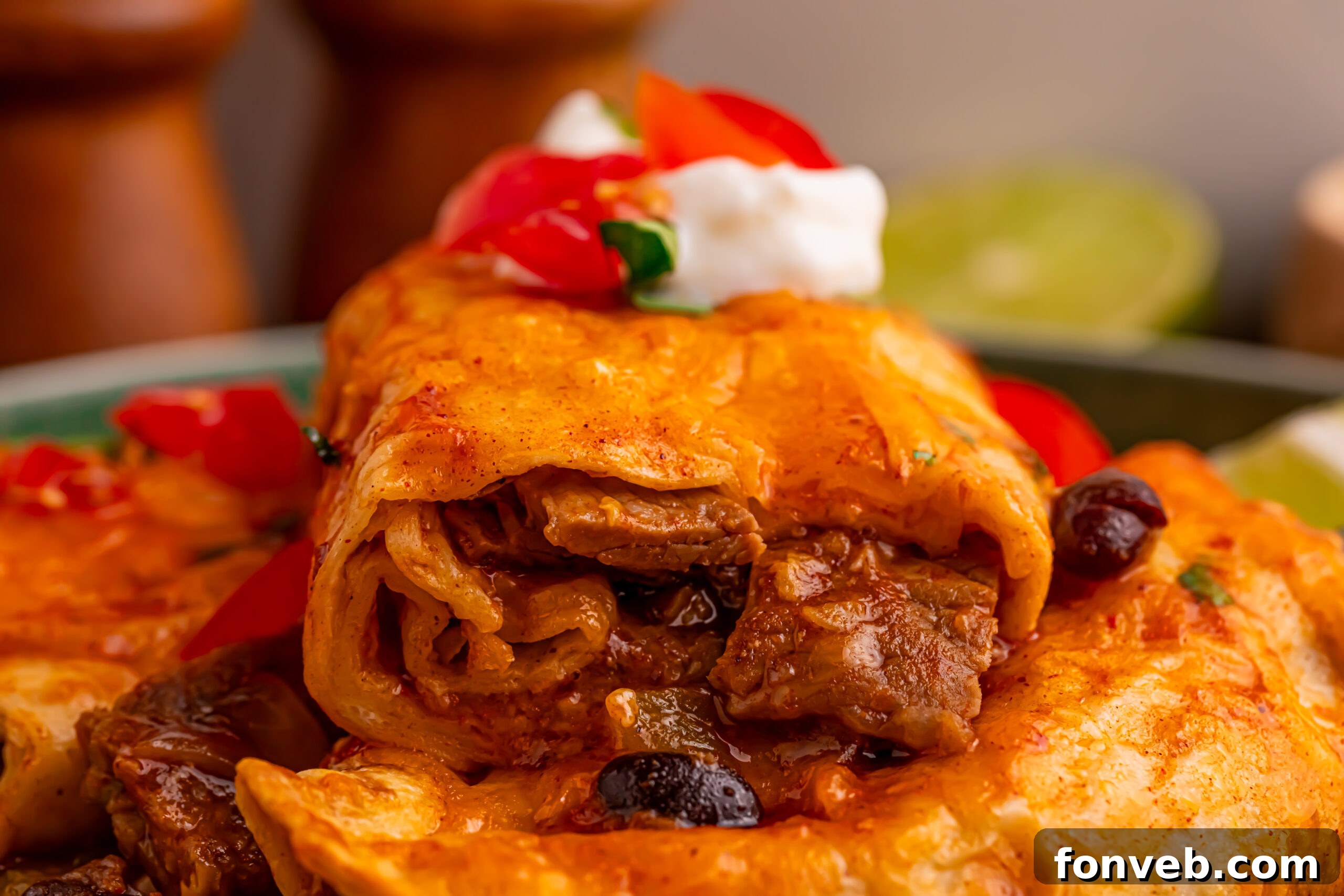 Steak Enchiladas on a green plate topped with sour cream and diced tomatoes 