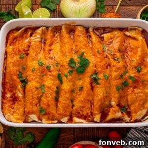 Steak Enchiladas in a casserole pan sitting on a wooden table with sliced limes, onion and cilantro behind the casserole dish