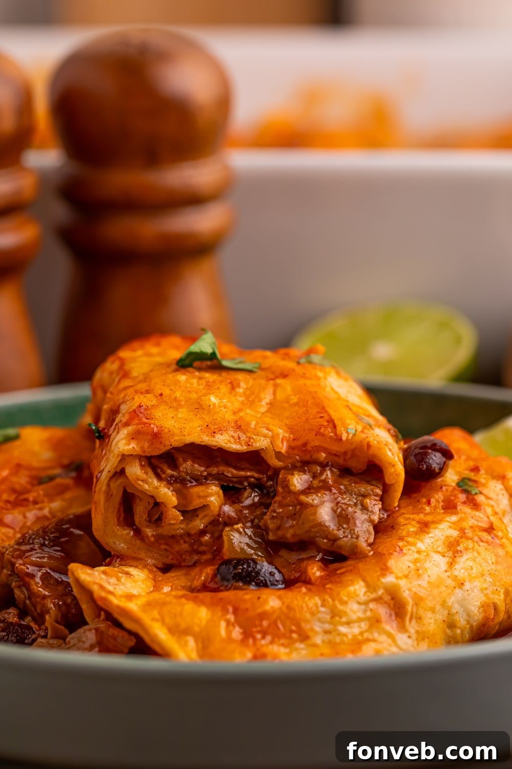 Steak Enchiladas on a grey plate on table with one cut in half sitting on top of more on a plate to show the filling of the enchiladas 