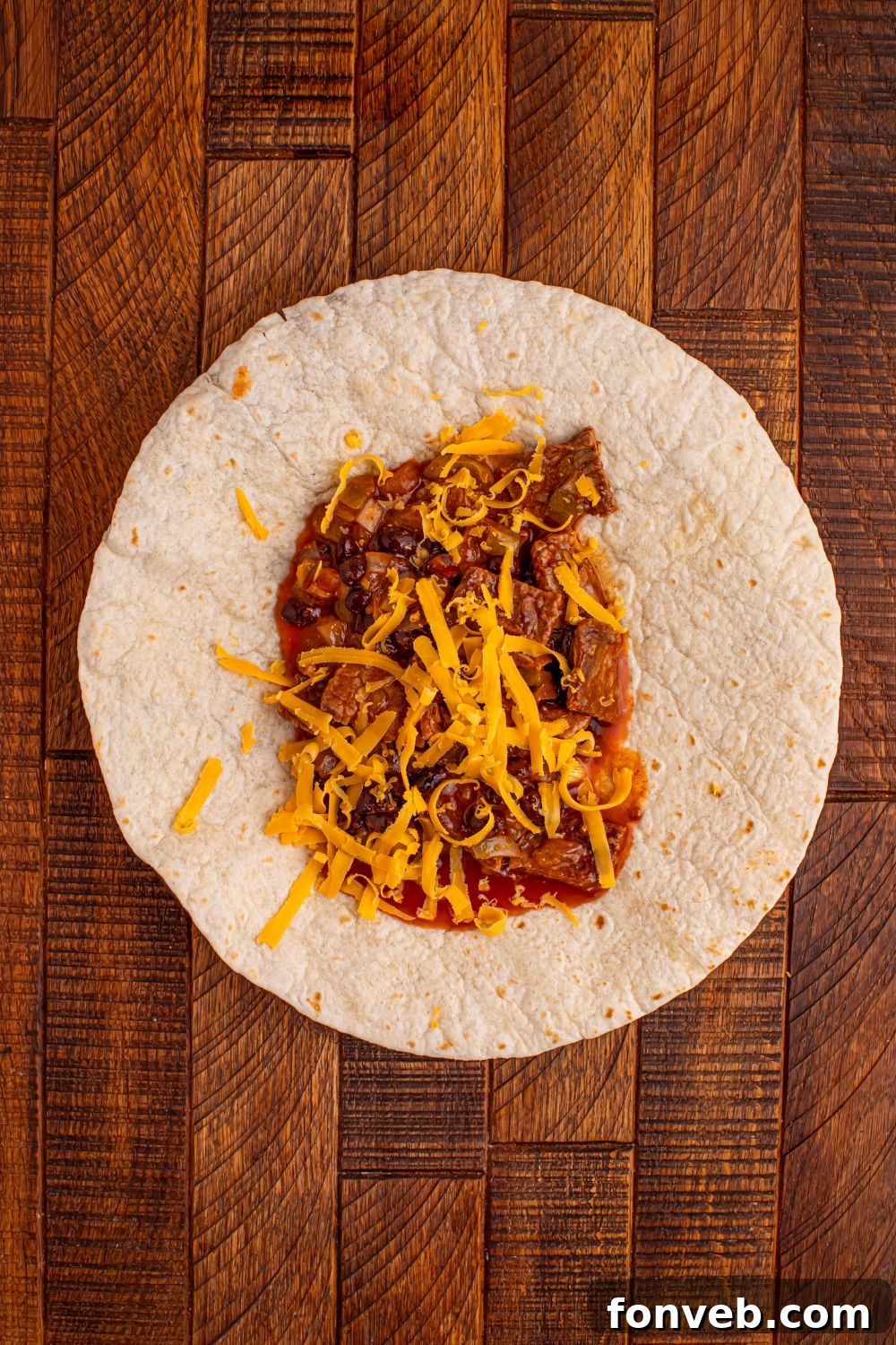 tortilla on wooden table full of a steak filling in center for making Steak Enchiladas