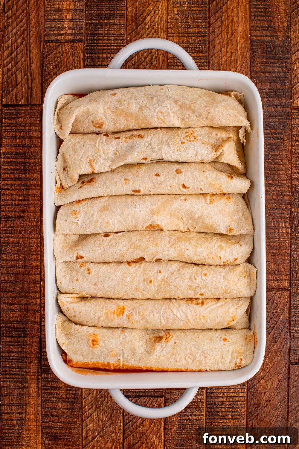 rolled enchiladas in a white casserole dish on a wooden table 