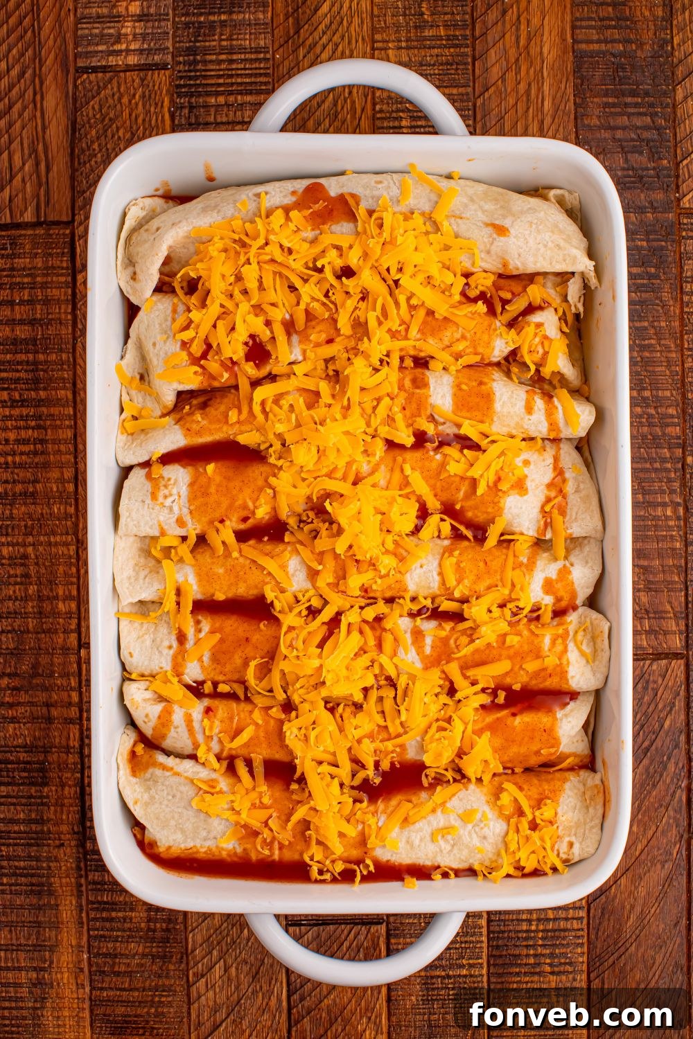 Steak Enchiladas being assembled and placed in a white casserole dish on the wooden table 