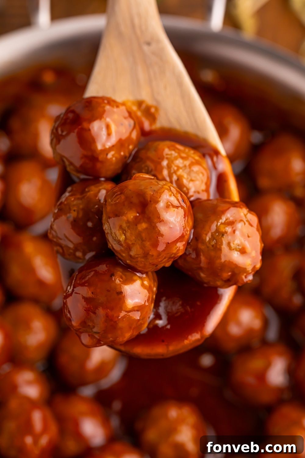 Peach BBQ Meatballs on a wooden spoon above a skillet on the table 