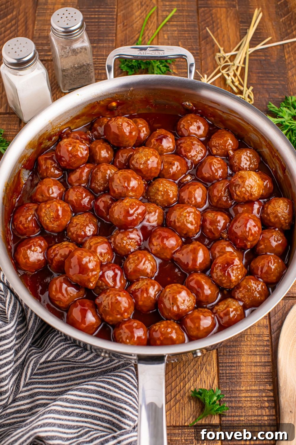 Peach BBQ Meatballs all saucy in a skillet on the table with a blue towel slightly under the pan 