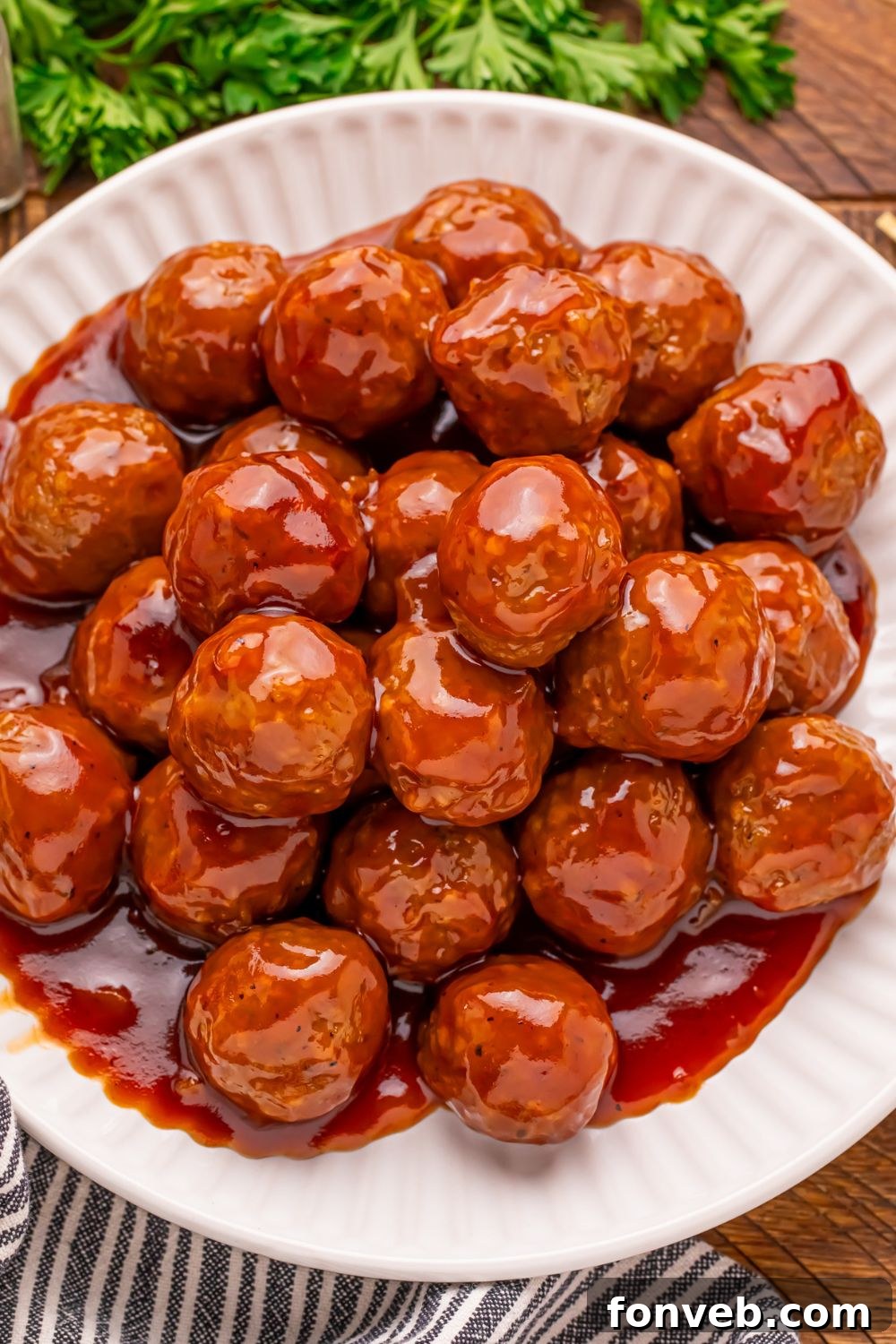 Peach BBQ Meatballs piled on a white plate on a wooden table with parsley to the side on table 