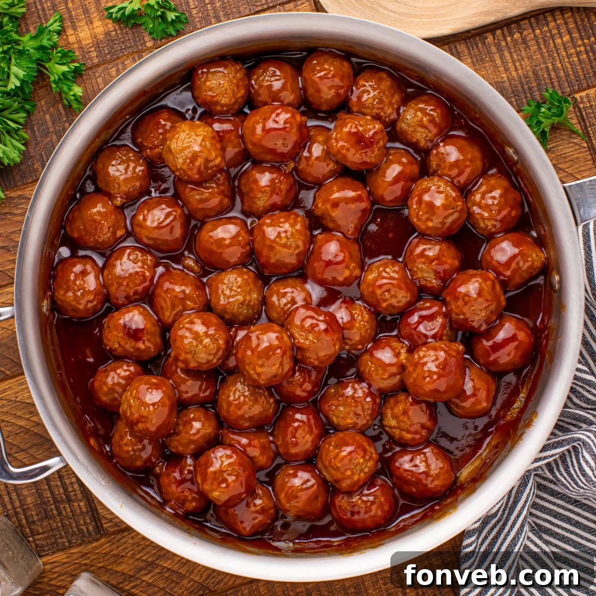 Peach BBQ Meatballs in a skillet on a wooden table with parsley to the side of it 