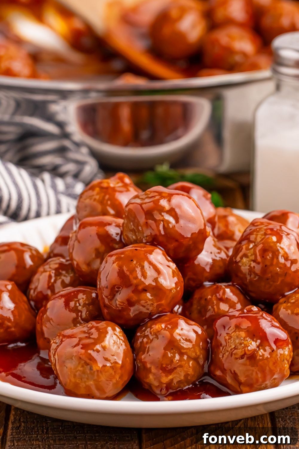 Peach BBQ Meatballs on a white plate on table with a skillet behind it on table with salt shaker to side and a towel 