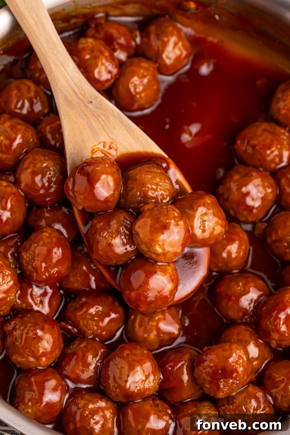 Peach BBQ Meatballs in a skillet with a wooden spoon scooping up some of the meatballs 