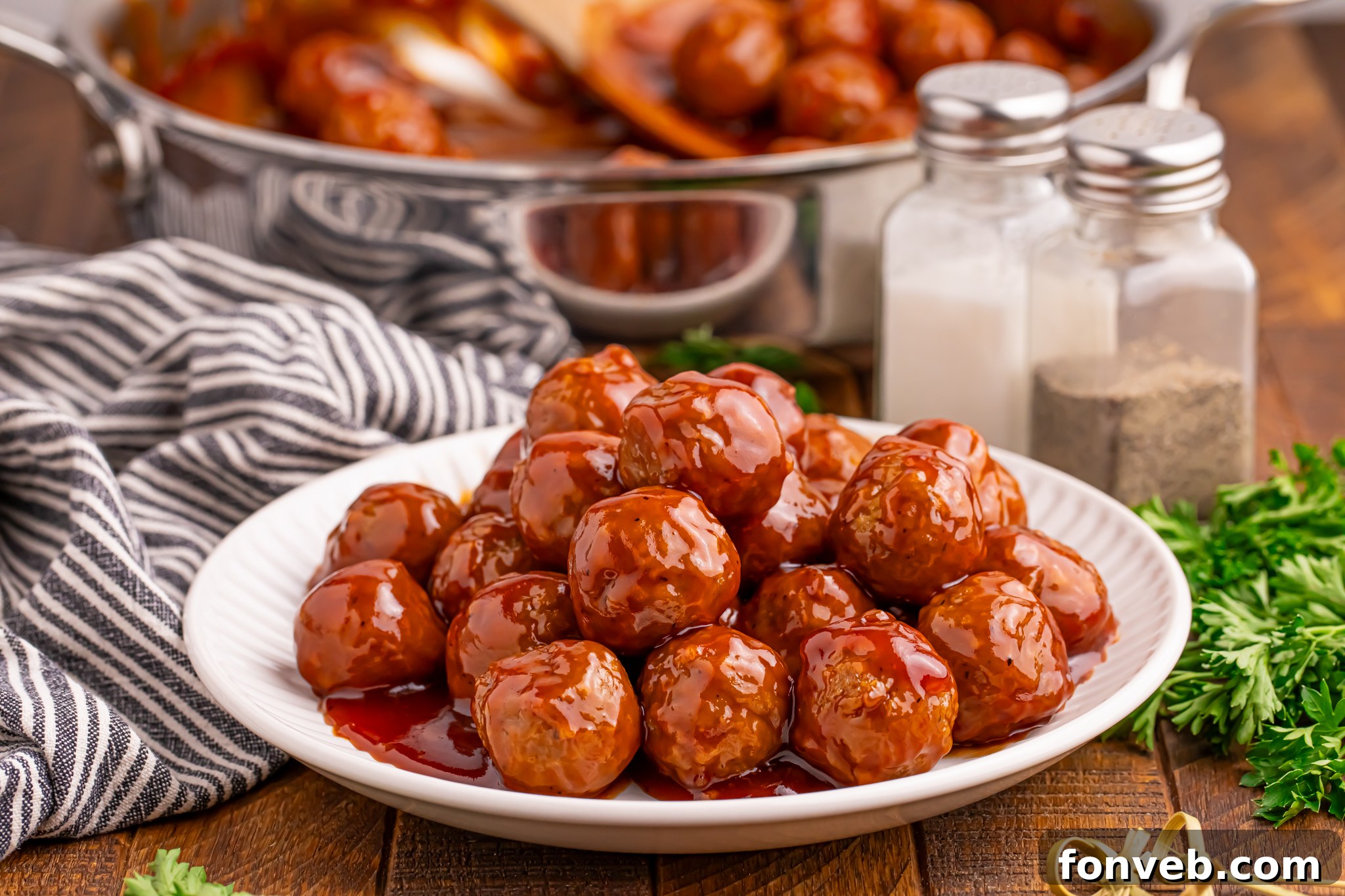 Peach BBQ Meatballs on a white plate on a dark wooden table with a skillet behind the plate 