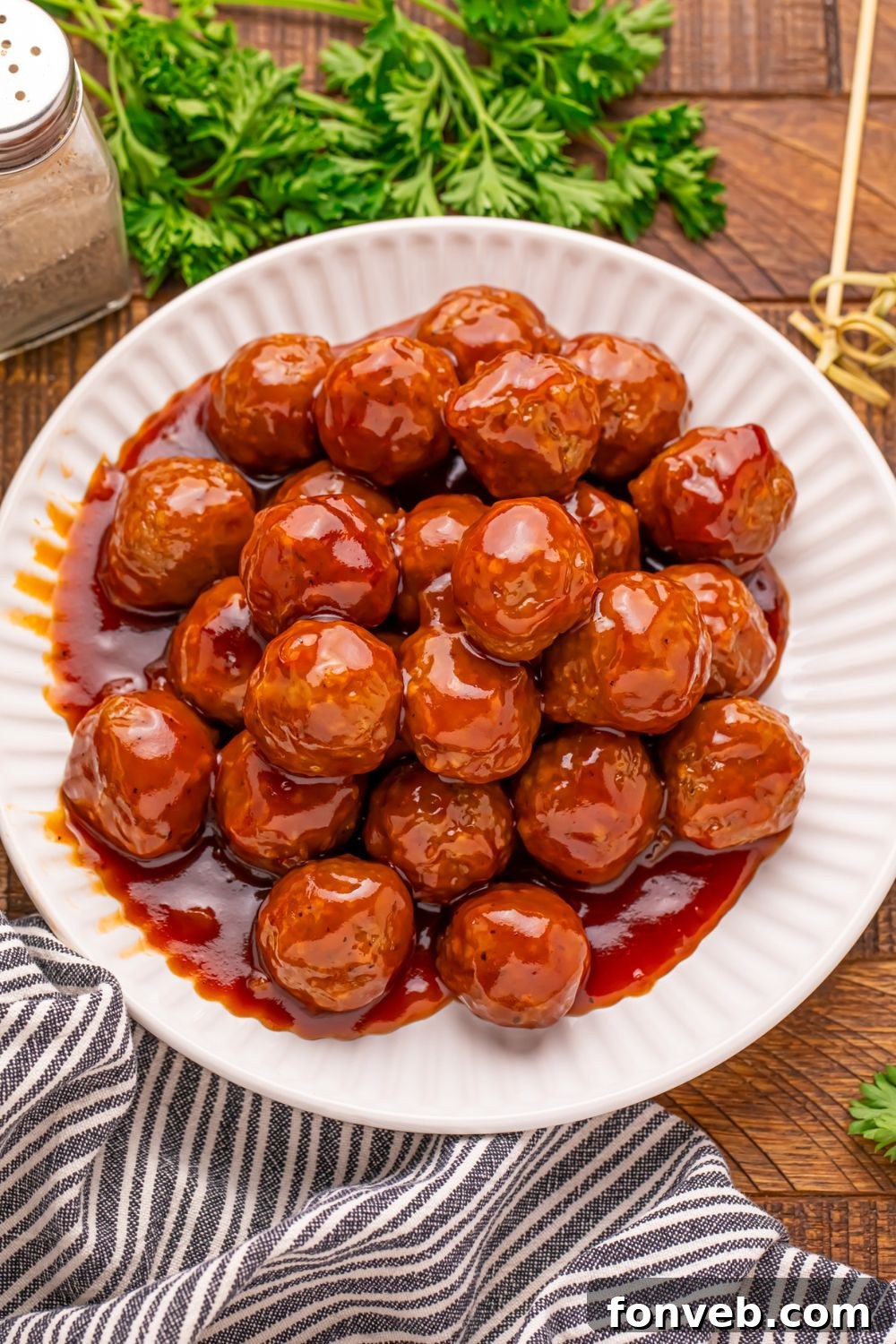 white plate full of Peach BBQ Meatballs sitting on table with a towel in front and parsley behind the plate 