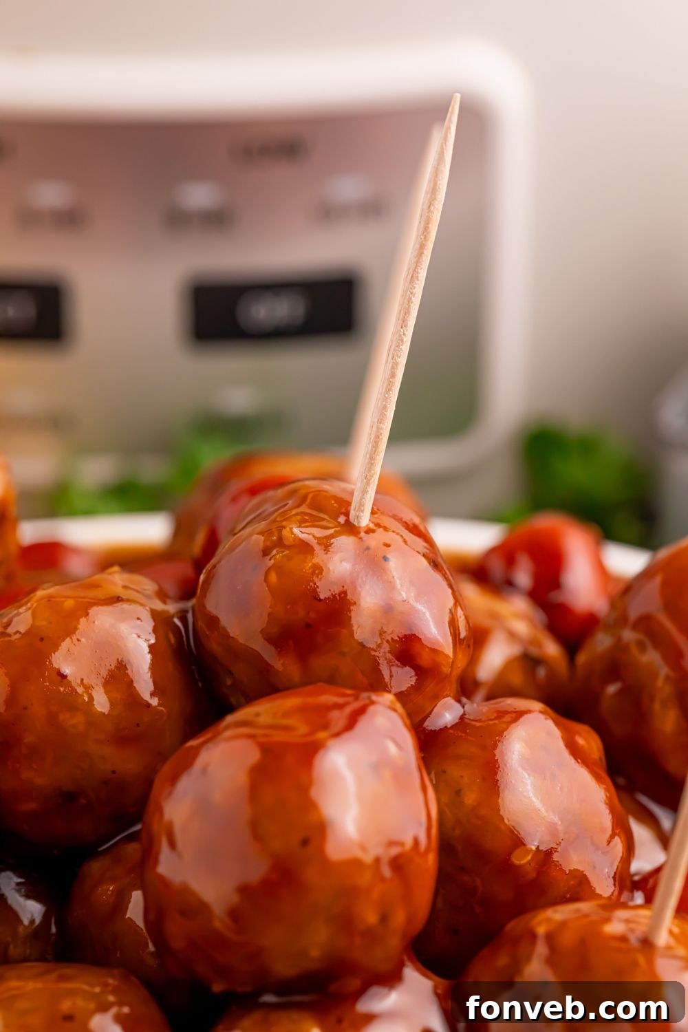 a bowl full of smokies and meatballs in sauce with a couple toothpicks poked into the meatballs 