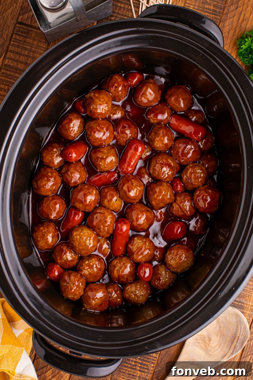 a black Crockpot full of Teriyaki BBQ Cocktail Meatballs & Lil Smokies with a wooden spoon to side on table and salt and pepper shakers 