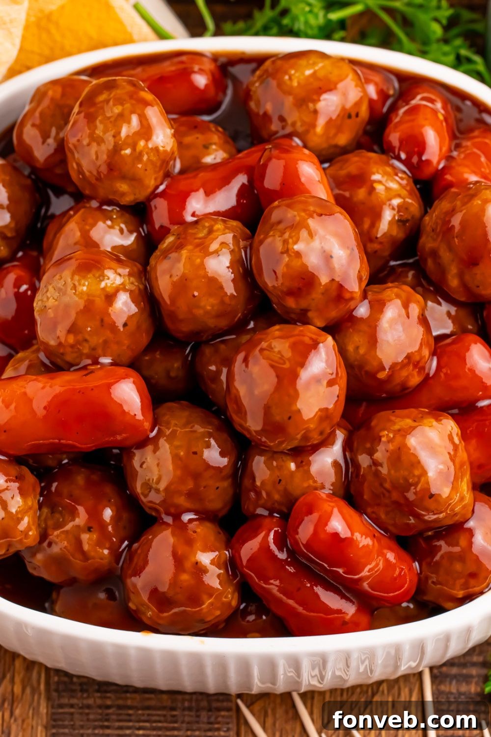 a white bowl full of Crockpot Teriyaki BBQ Cocktail Meatballs & Lil Smokies with some parsley behind it on the table 