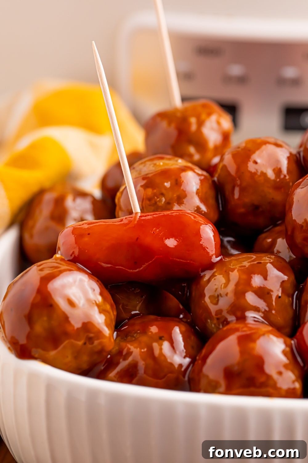 Crockpot Teriyaki BBQ Cocktail Meatballs & Lil Smokies mixture in a white bowl on table with a yellow towel behind it on the table 