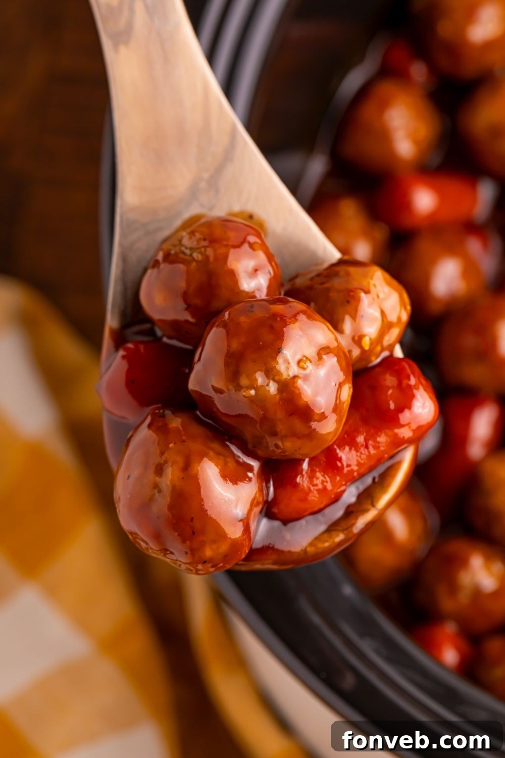 Crockpot Teriyaki BBQ Cocktail Meatballs & Lil Smokies on a wooden spoon above the crockpot on the wooden table 
