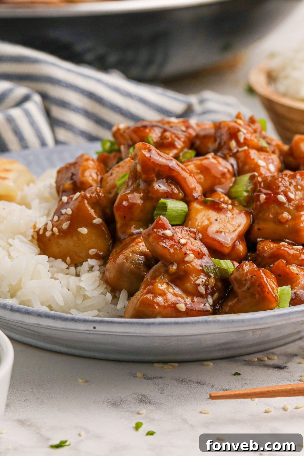 Irresistible Bourbon Chicken Skillet Quick Weeknight Win 11 plate with some diced bourbon chicken ad a side of rice to side with a striped grey towel behind it on the table