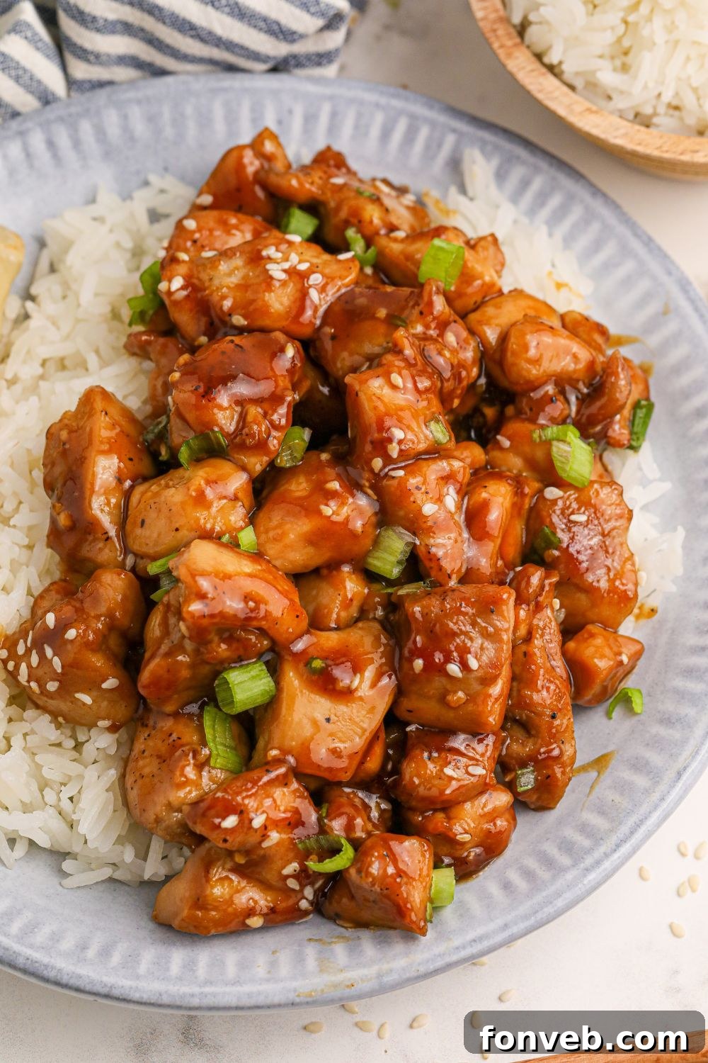Irresistible Bourbon Chicken Skillet Quick Weeknight Win 12 looking down on table with a plate full of diced skillet bourbon chicken and a bed of rice to the side and a red and grey striped towel to side