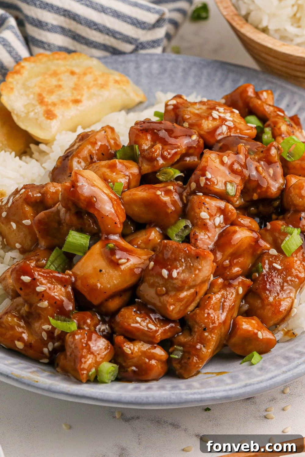 Irresistible Bourbon Chicken Skillet Quick Weeknight Win 15 close up look of all the bourbon chicken on a blue plate on the table with some rice to the side of the plate and a bowl of more rice behind the plate