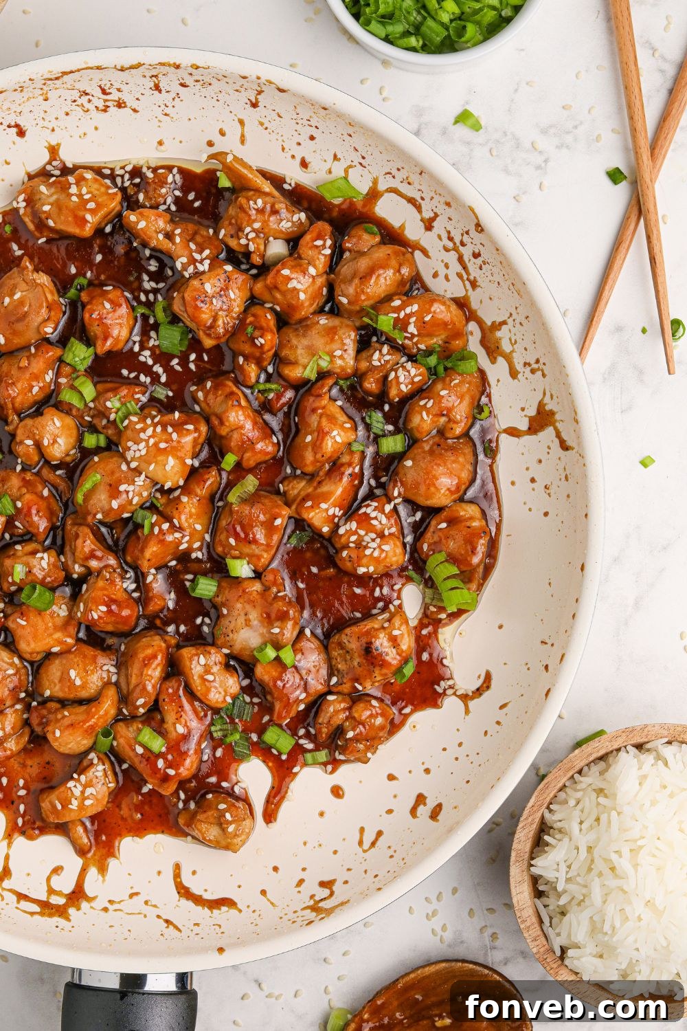 Irresistible Bourbon Chicken Skillet Quick Weeknight Win 18 a white skillet full of saucy bourbon chicken on a table with chopsticks to the side and a bowl of rice to the side of the pan