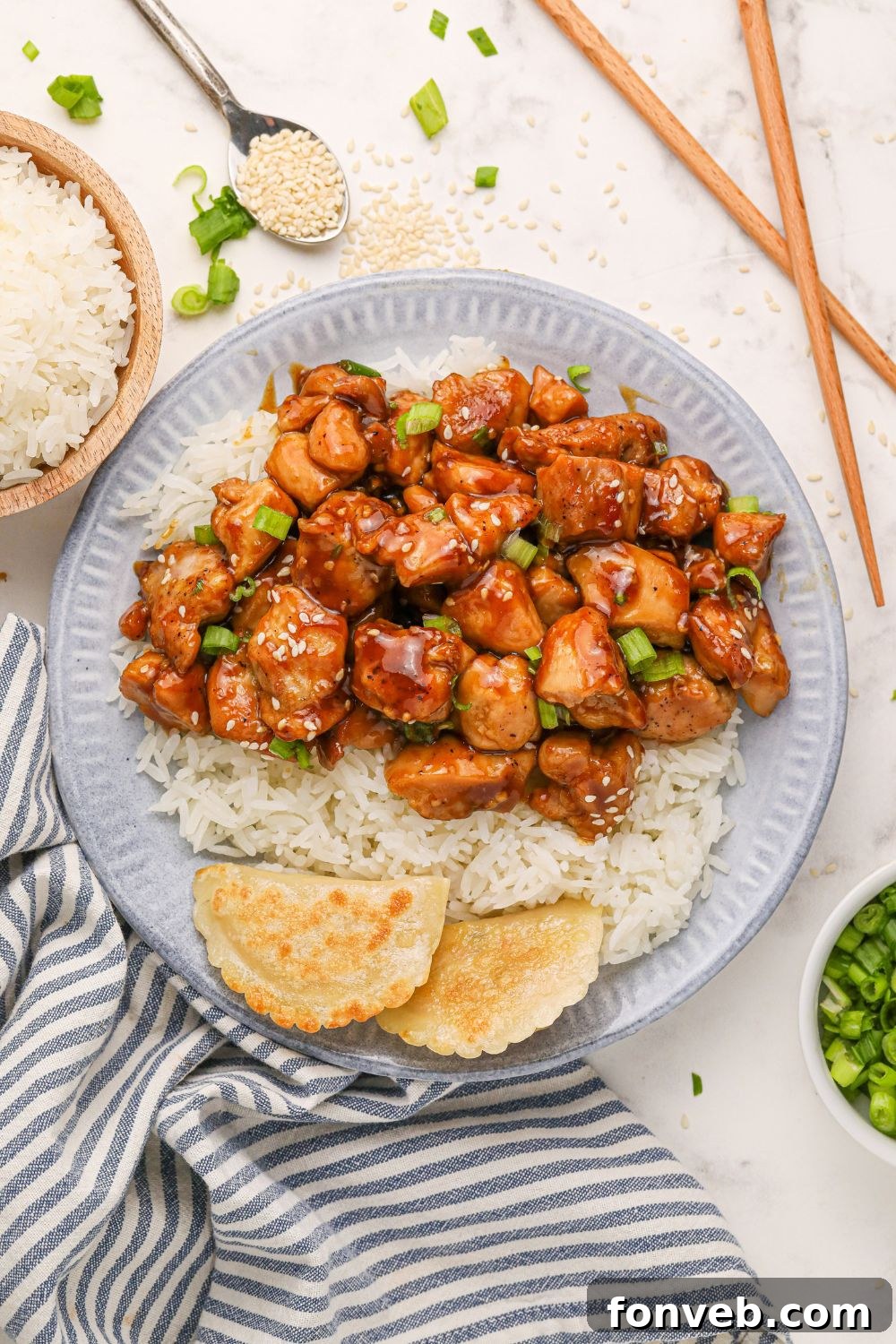 Irresistible Bourbon Chicken Skillet Quick Weeknight Win 21 looking down on table with a grey plate with bourbon chicken, rice, and pieorgies to side and a bowl of rice and green onions to side on the table