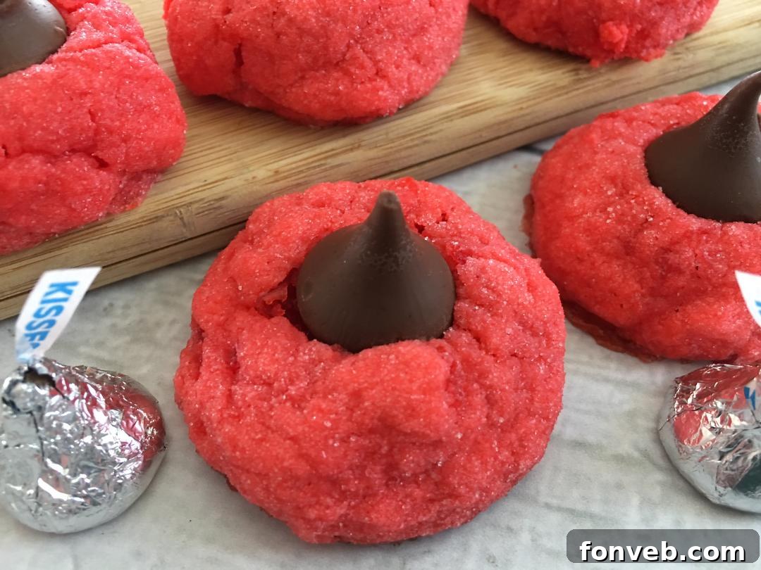 Cherry Kiss Cookies cooling on parchment paper on a baking sheet, with several cookies already topped with chocolate kisses.
