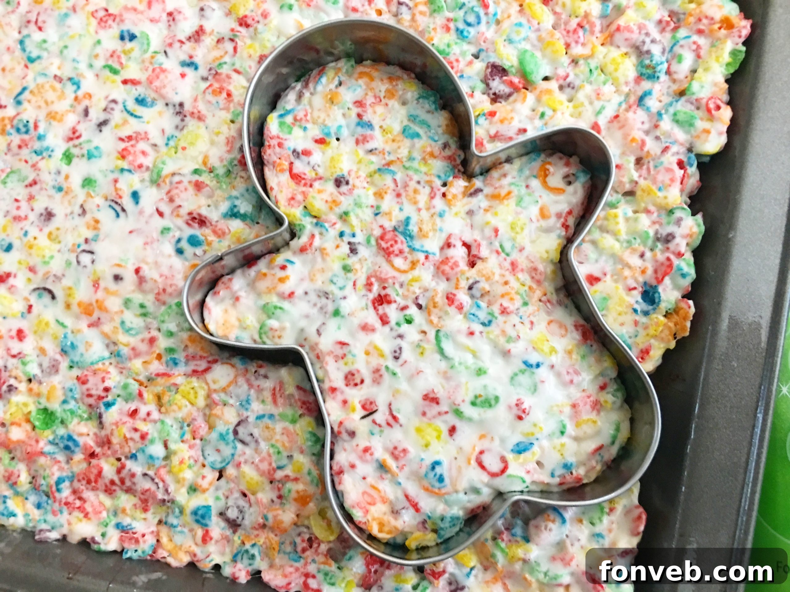 A child's hands carefully decorating a gingerbread-shaped Fruity Pebbles treat with frosting.