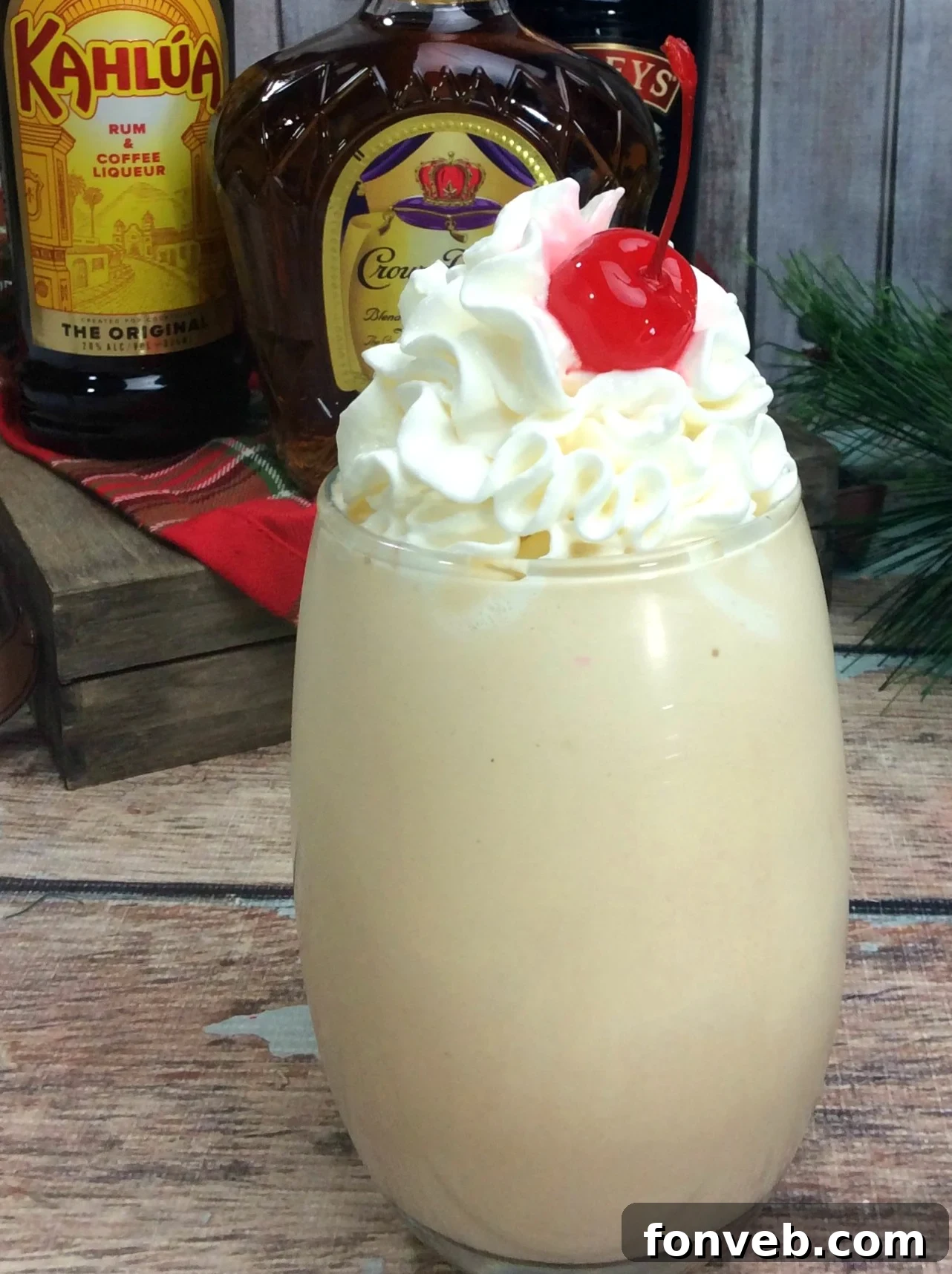 Delicious Alaska Duck Fart Cocktail in a tall glass, garnished with whipped cream and a cherry, against a blurred background.