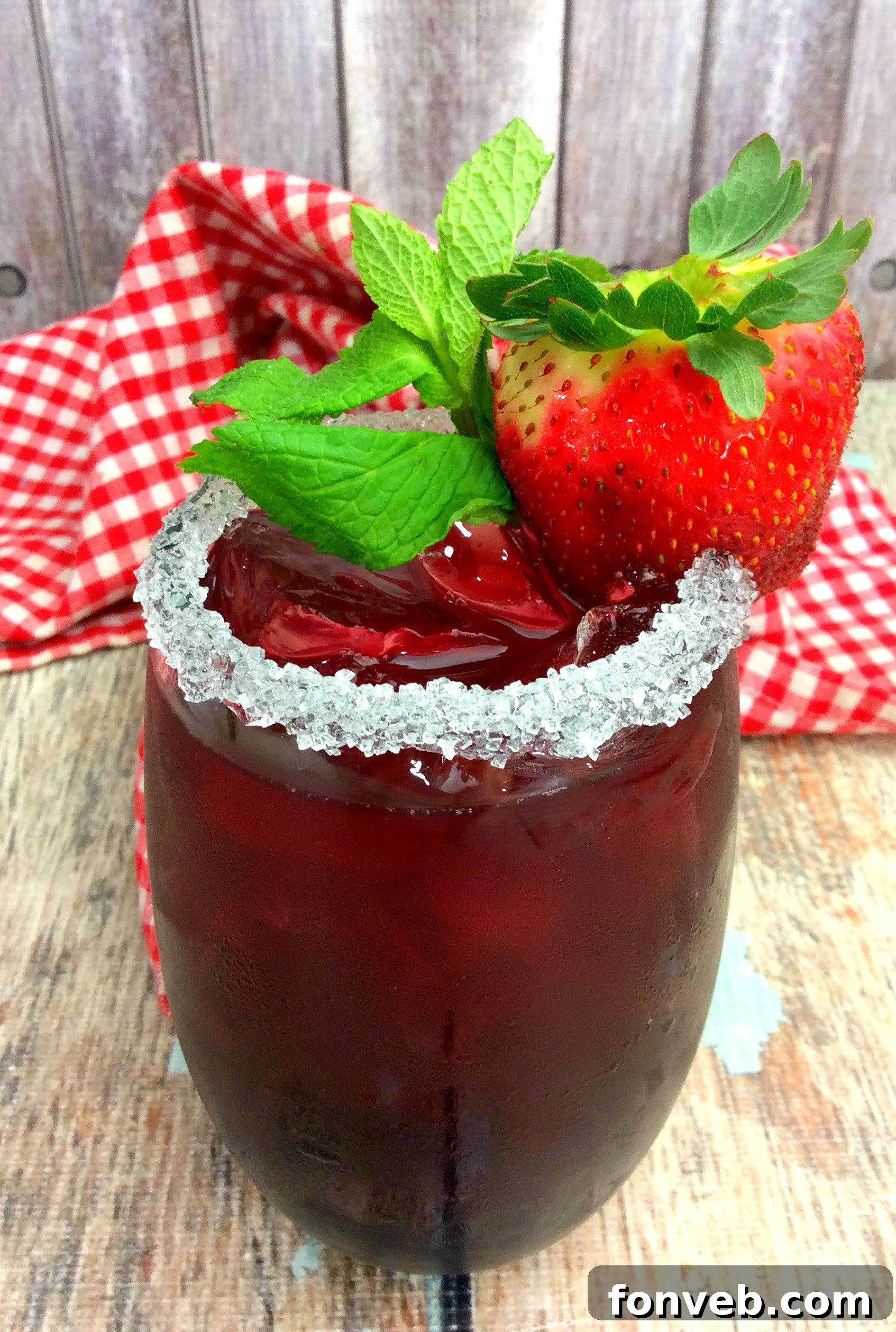 Close-up of Tickle Me Strawberry Triple Crown Cocktail, showing muddled ingredients at the bottom and a fresh strawberry garnish.