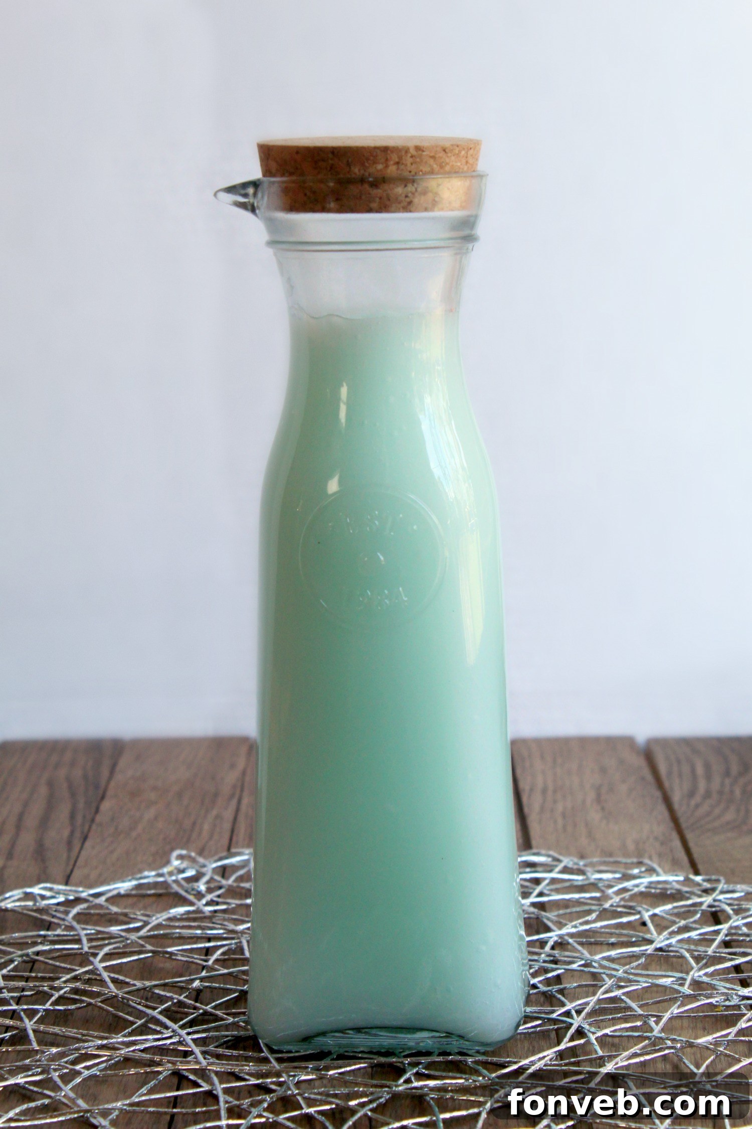 Homemade fabric softener in a bottle, ready to use, next to a basket of clean laundry