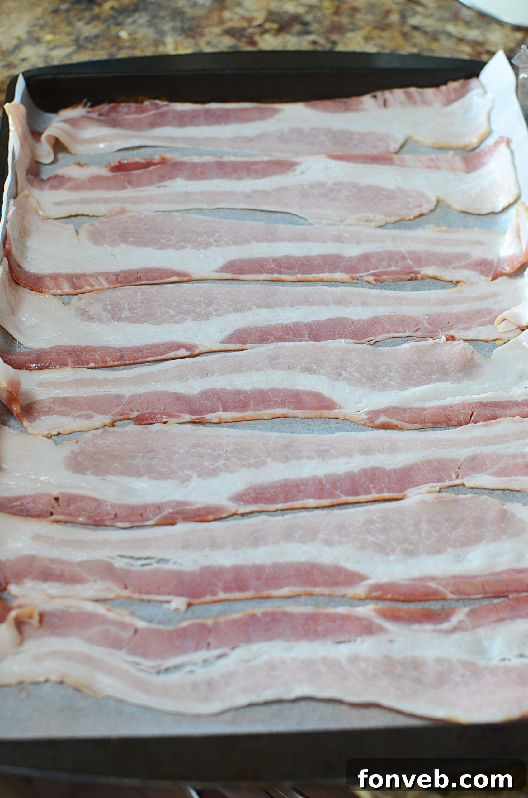 Raw bacon slices arranged in a single layer on a parchment-lined baking sheet, ready for the oven