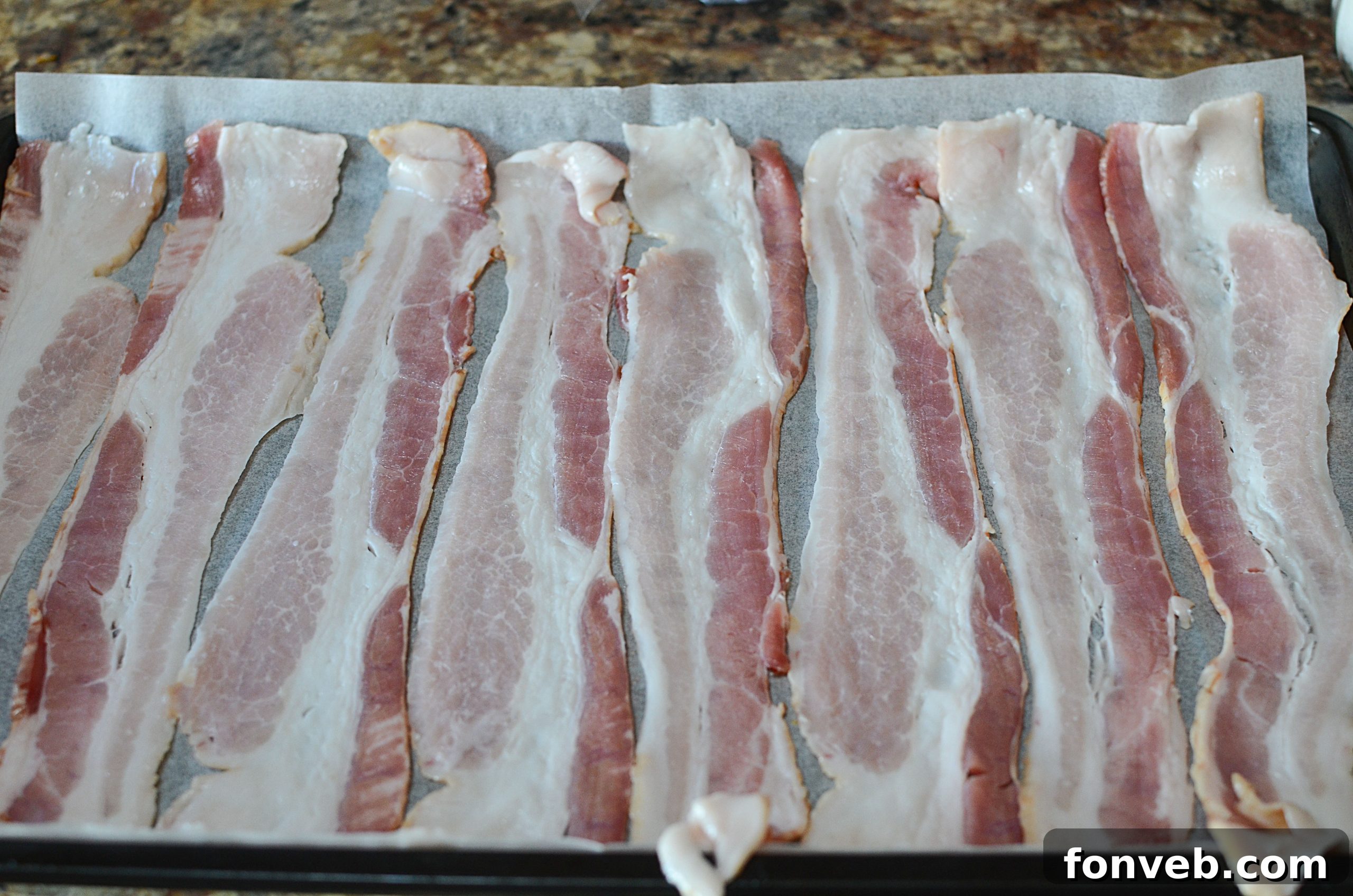 Bacon slices neatly arranged side-by-side on a baking sheet, ready for the oven