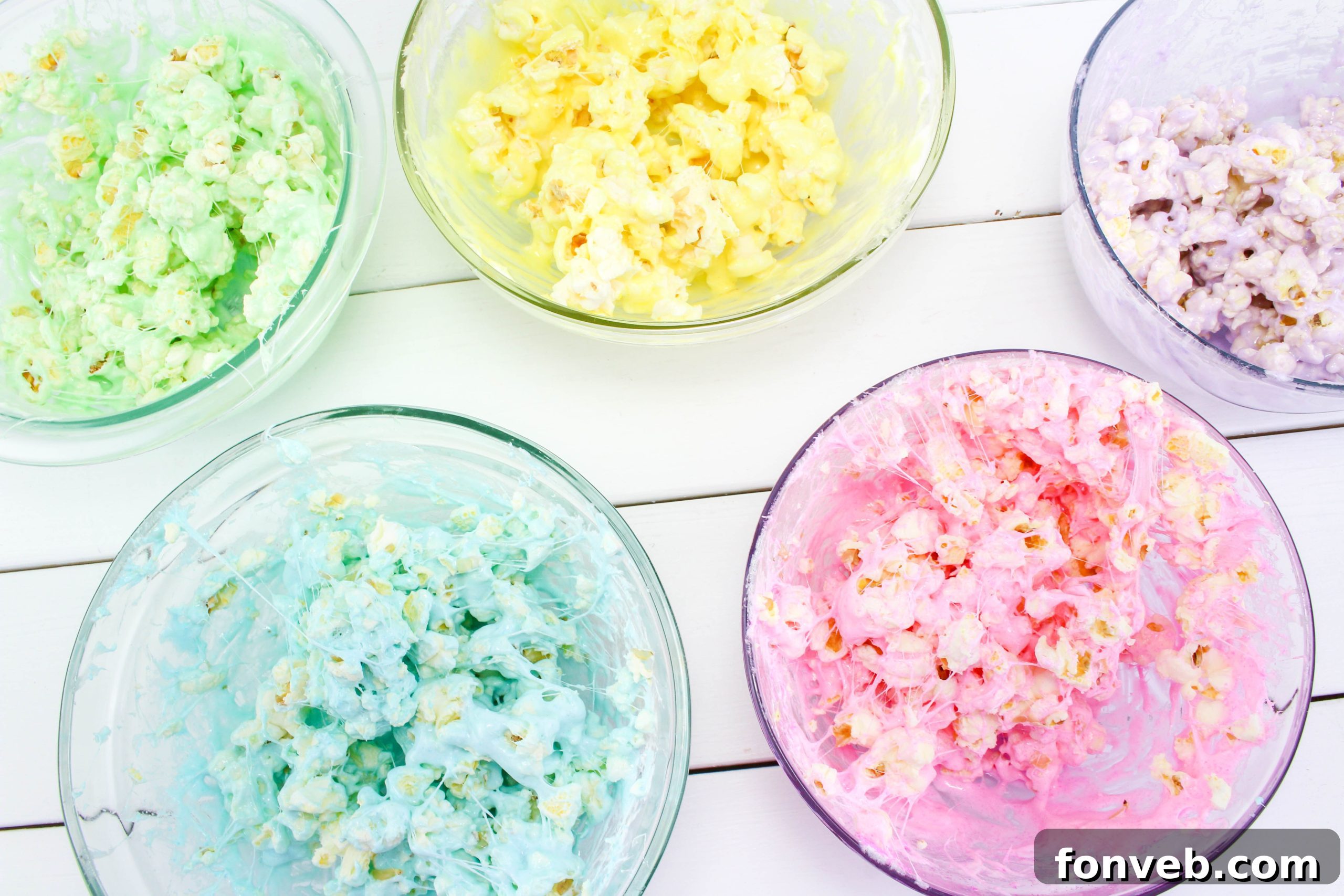 A hand gently shaping a multi-colored marshmallow popcorn ball, illustrating the simple and fun technique for creation.