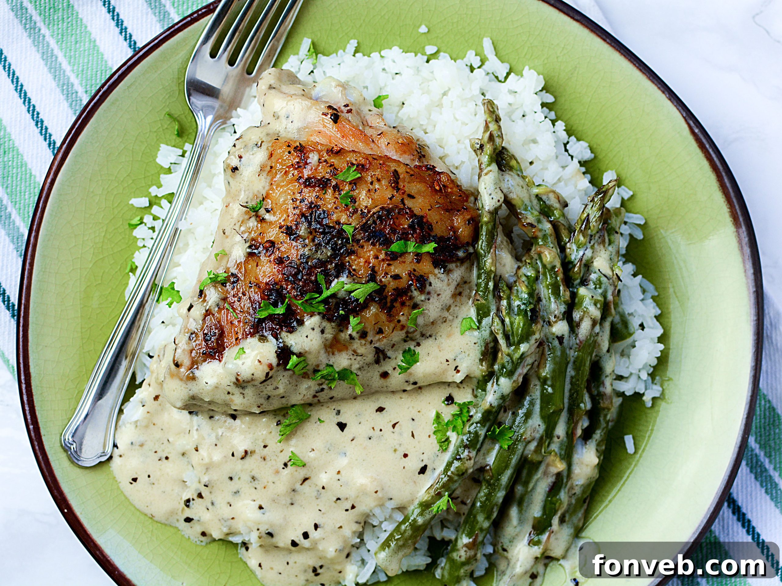 A close-up view of the perfectly cooked Creamy Garlic Dream Chicken nestled in its rich sauce with fresh asparagus