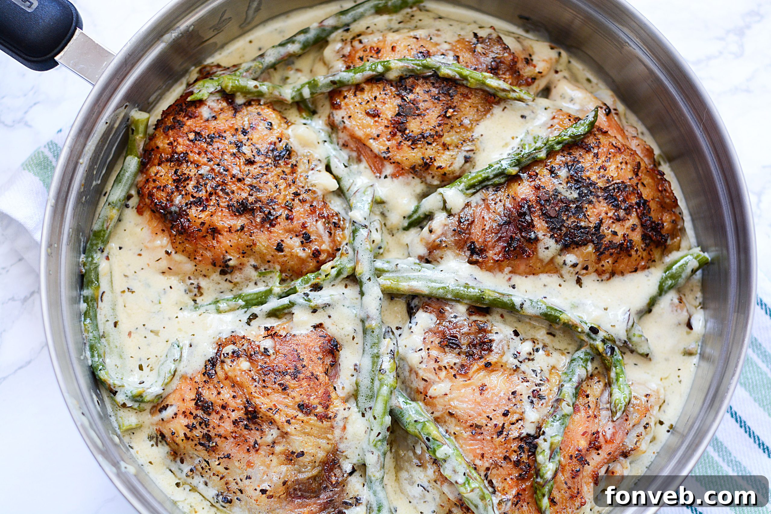 A wider shot of the skillet with Creamy Garlic Dream Chicken and Asparagus, showcasing the complete dish