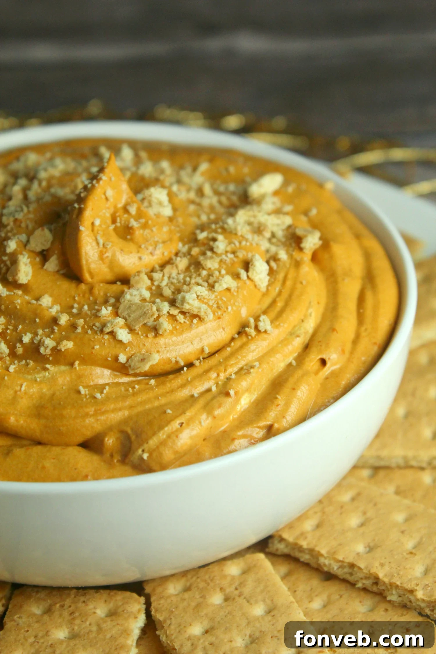 A vibrant, creamy pumpkin pie cheesecake dip served in a rustic bowl, garnished with a sprinkle of cinnamon, ready for dipping.