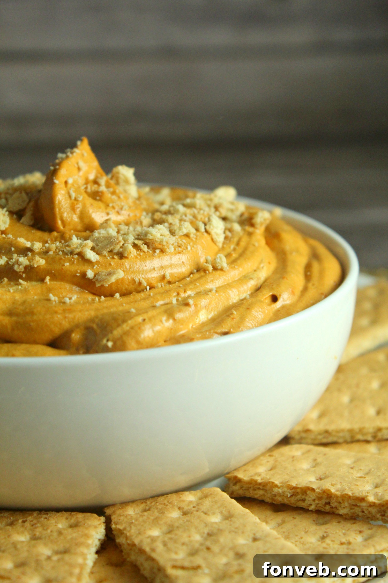 A close-up of a spoon dipping into the smooth, orange pumpkin pie cheesecake dip, highlighting its creamy texture.