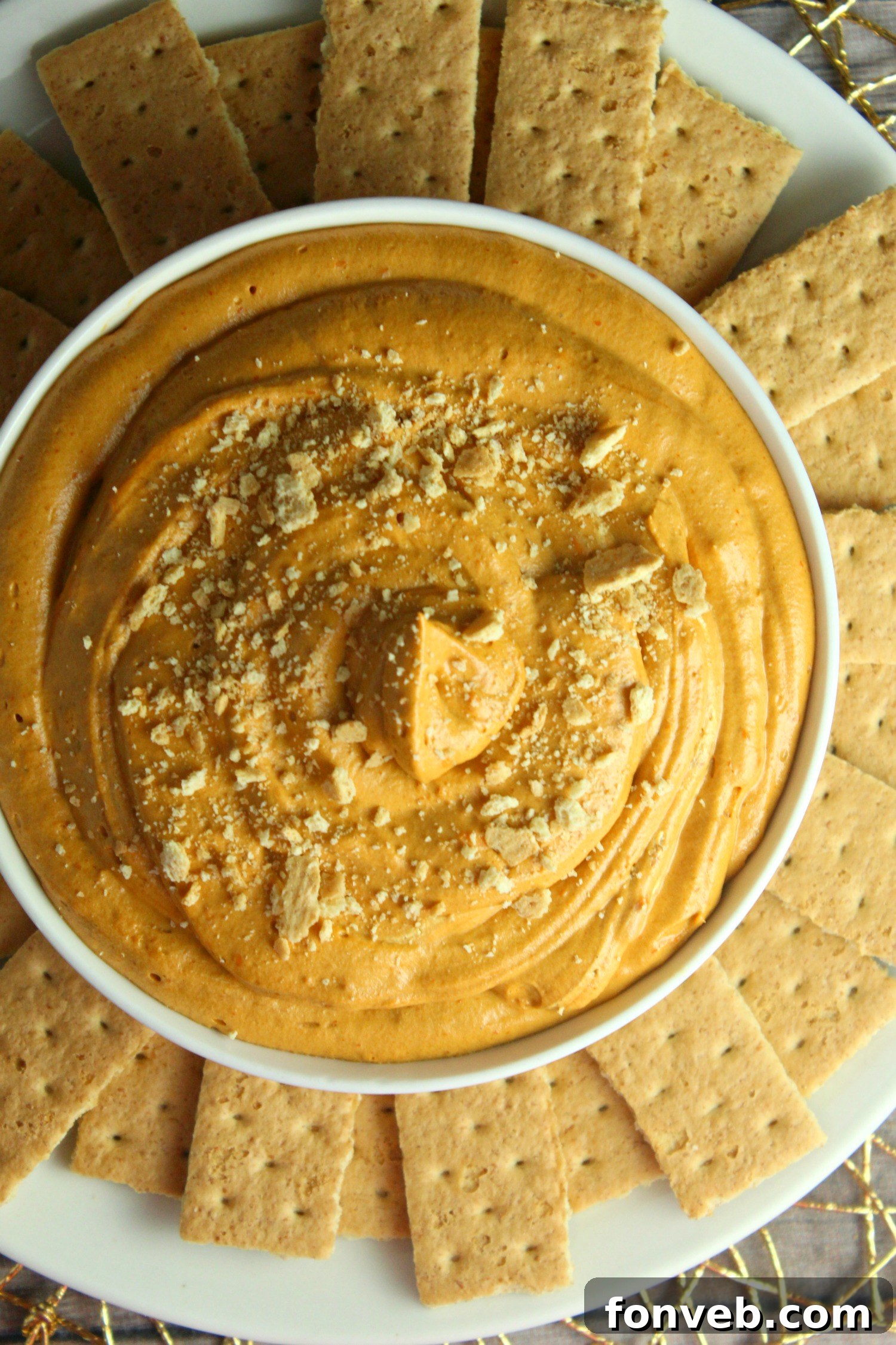 A beautifully styled serving of pumpkin pie cheesecake dip in a festive bowl, with various dippers arranged artfully around it on a wooden board.