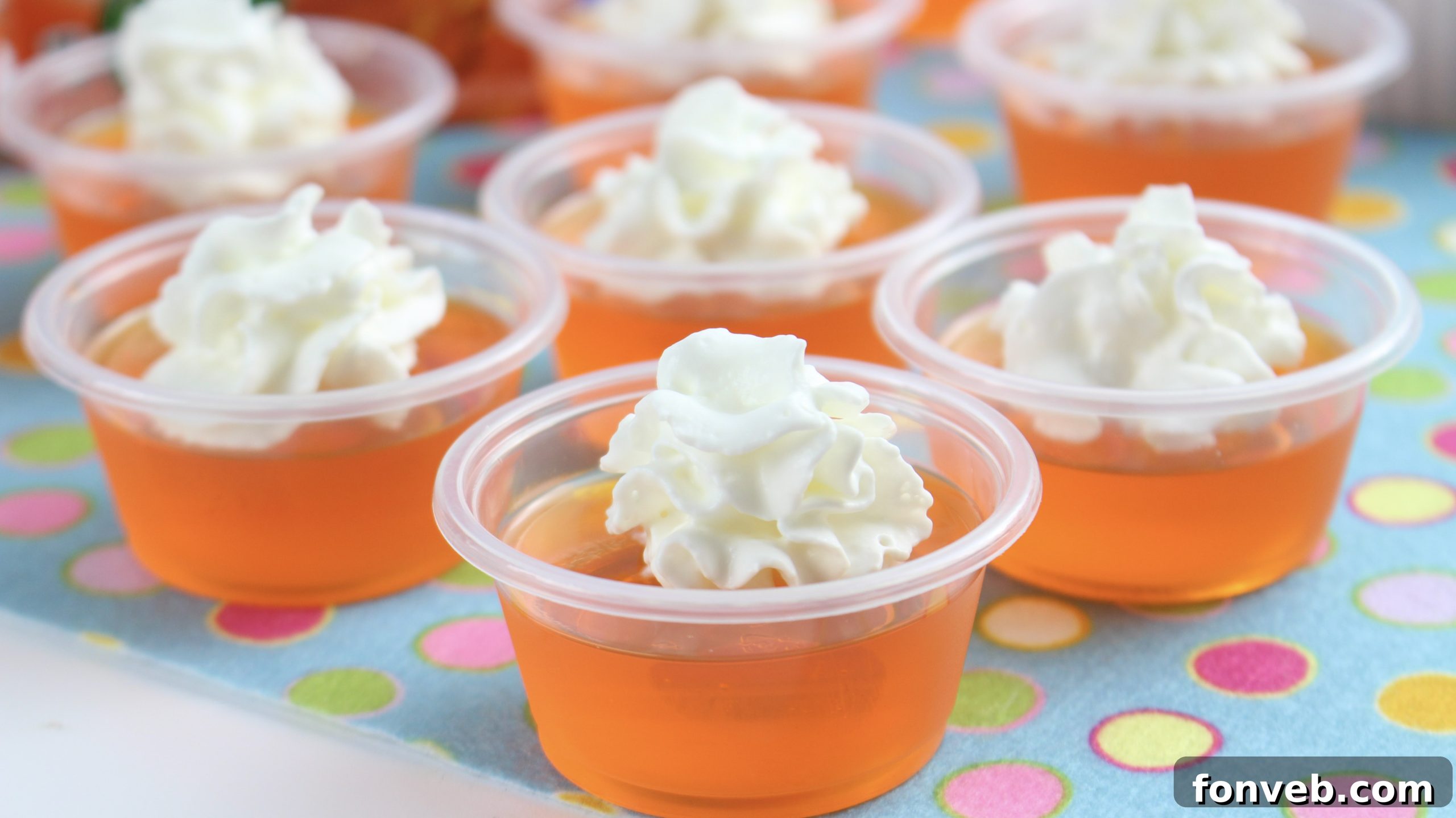 A hand holding an Orange Creamsicle Jello Shot with whipped cream, showing its irresistible appeal.