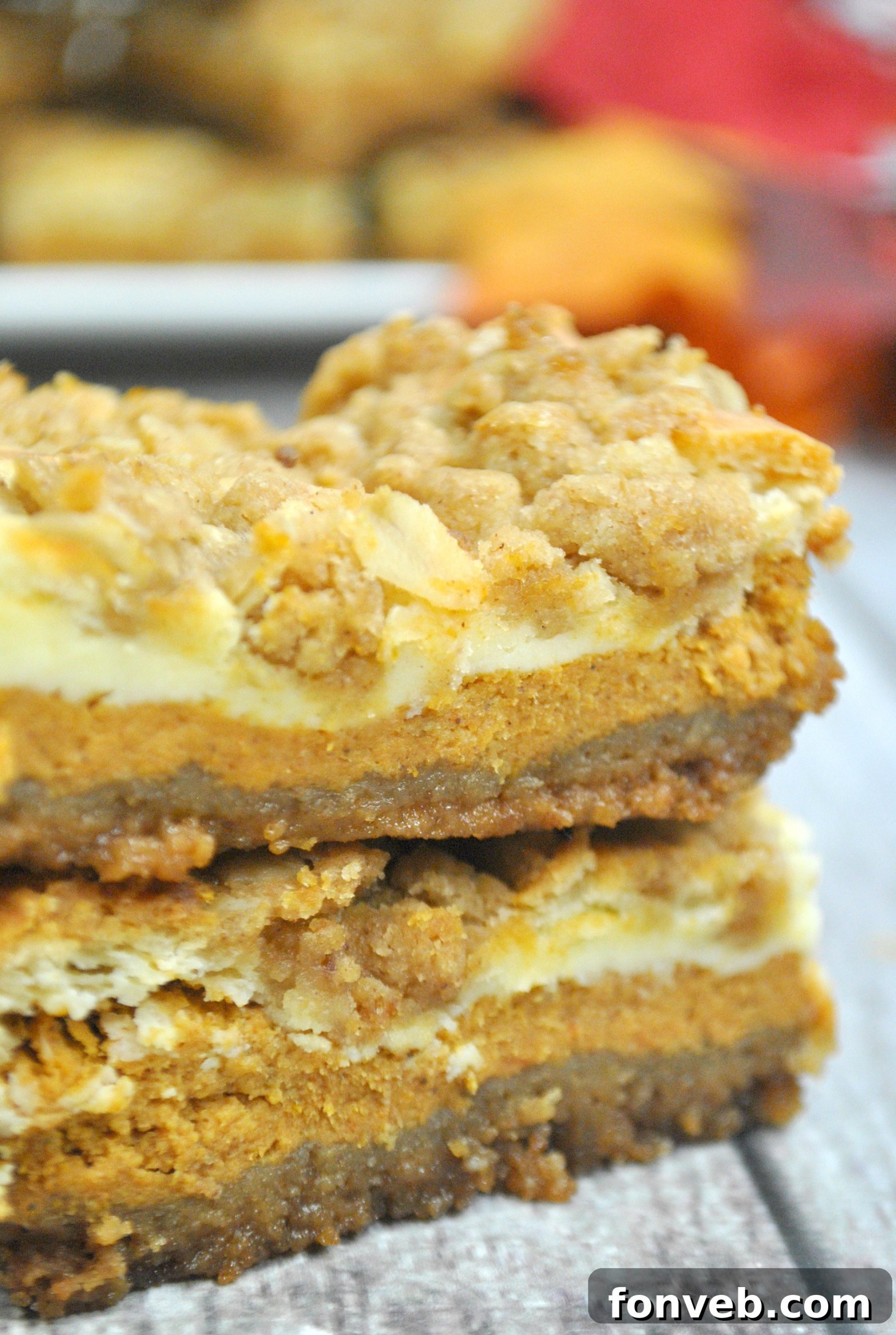 Harvest Pumpkin Crumble Cheesecake Squares 5 A close-up, side-angle view of a single pumpkin cheesecake bar, clearly showing the distinct layers of graham cracker crust, light cheesecake, pumpkin cheesecake, and thick streusel.