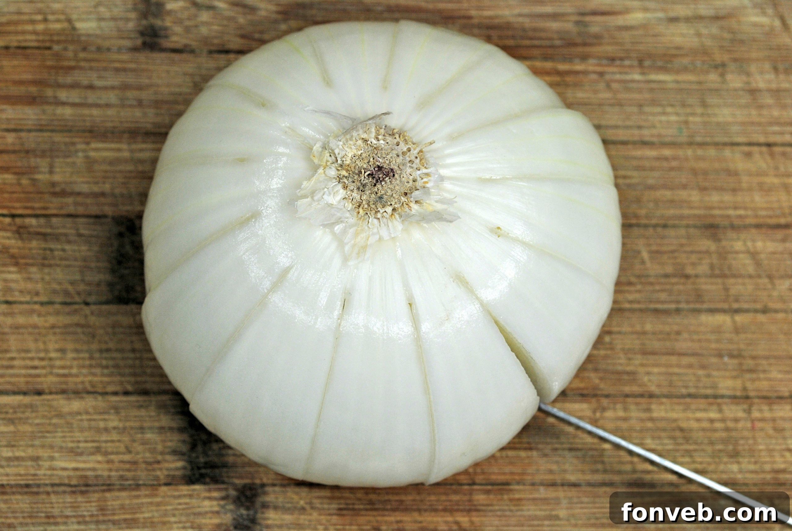 A large, unpeeled Vidalia onion sitting on a cutting board, prepared to be transformed into a blooming shape.