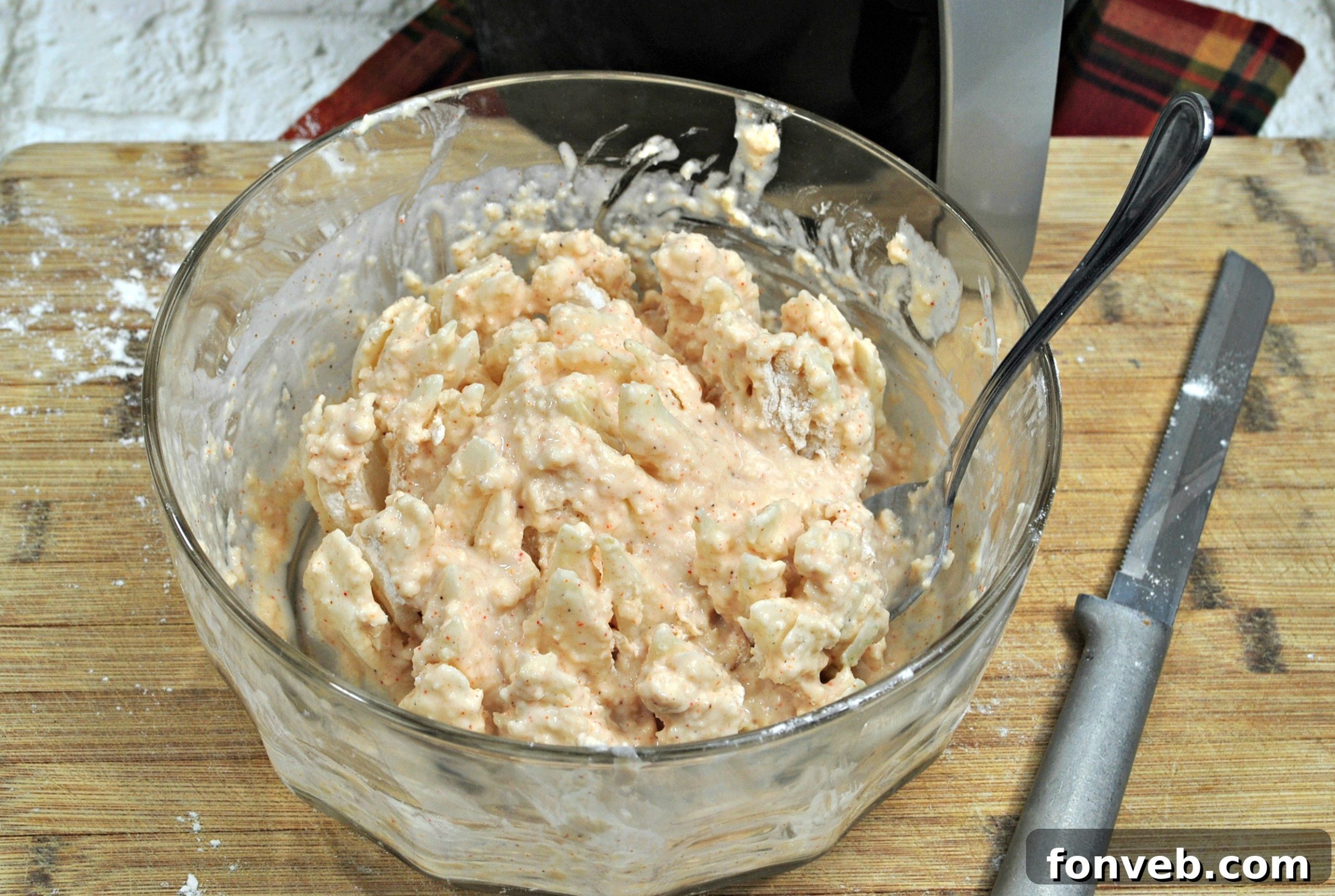 A bloomed onion being carefully coated by hand with the rich, spiced batter, ensuring even and complete coverage on all petals.