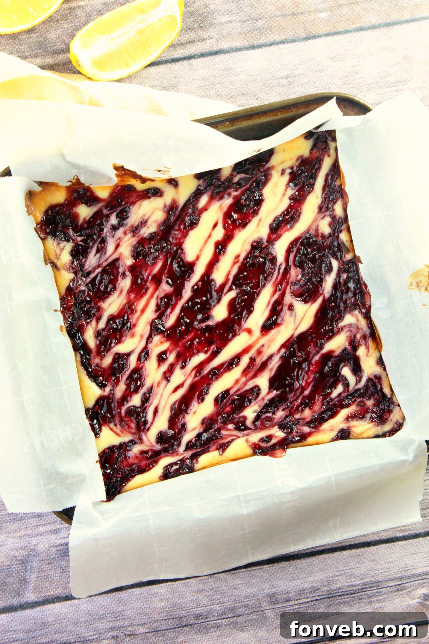 Two perfectly sliced lemon raspberry cheesecake bars with a fork poised to take a bite, showcasing the distinct layers of golden graham cracker crust, thick creamy cheesecake, and vibrant raspberry topping.
