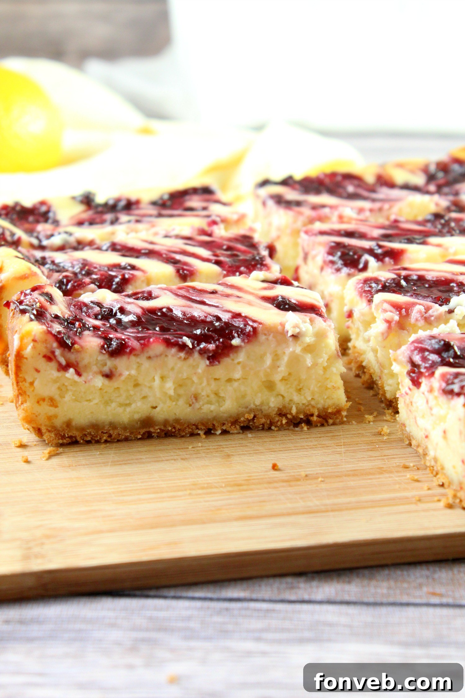 A delicious slice of lemon raspberry cheesecake bar being carefully lifted from the baking pan with a spatula, revealing the distinct layers of crust, cheesecake, and raspberry swirl.