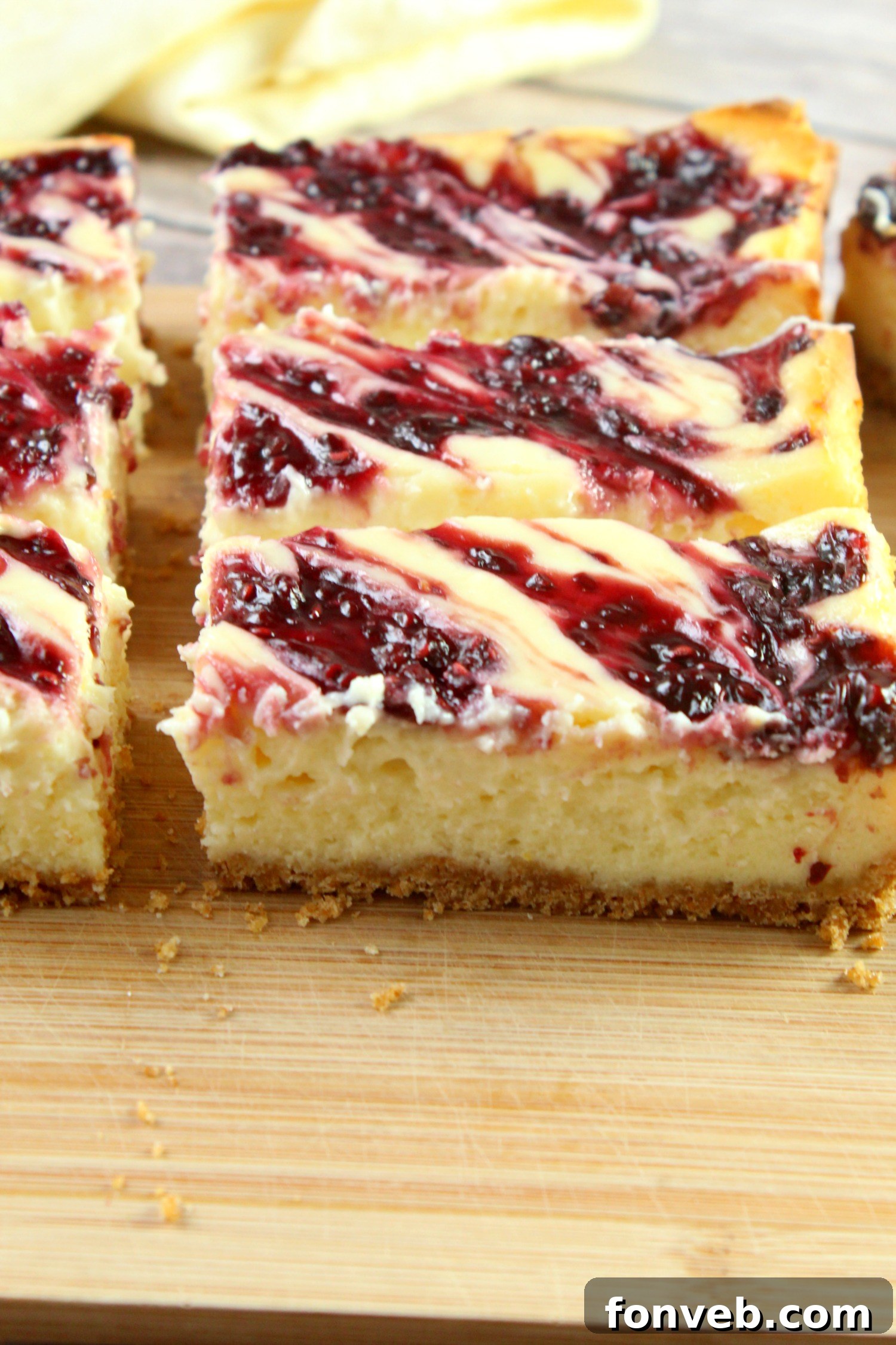 A neatly arranged row of perfectly cut lemon raspberry cheesecake bars sitting in a baking pan, showcasing their readiness to be served and enjoyed by guests.