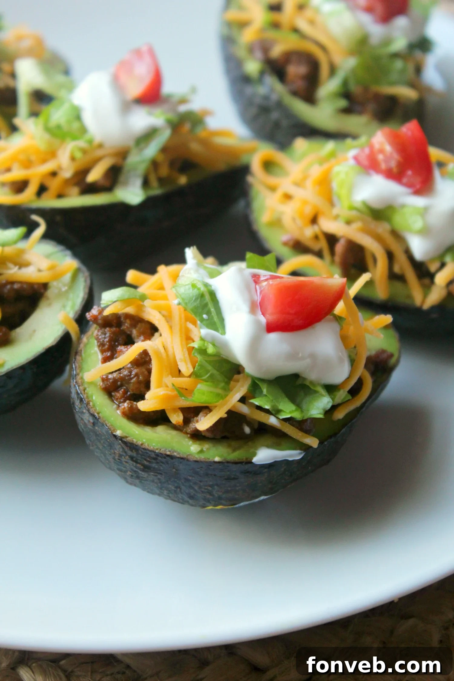Two halves of taco stuffed avocados, garnished with sour cream and cilantro, presented on a white plate