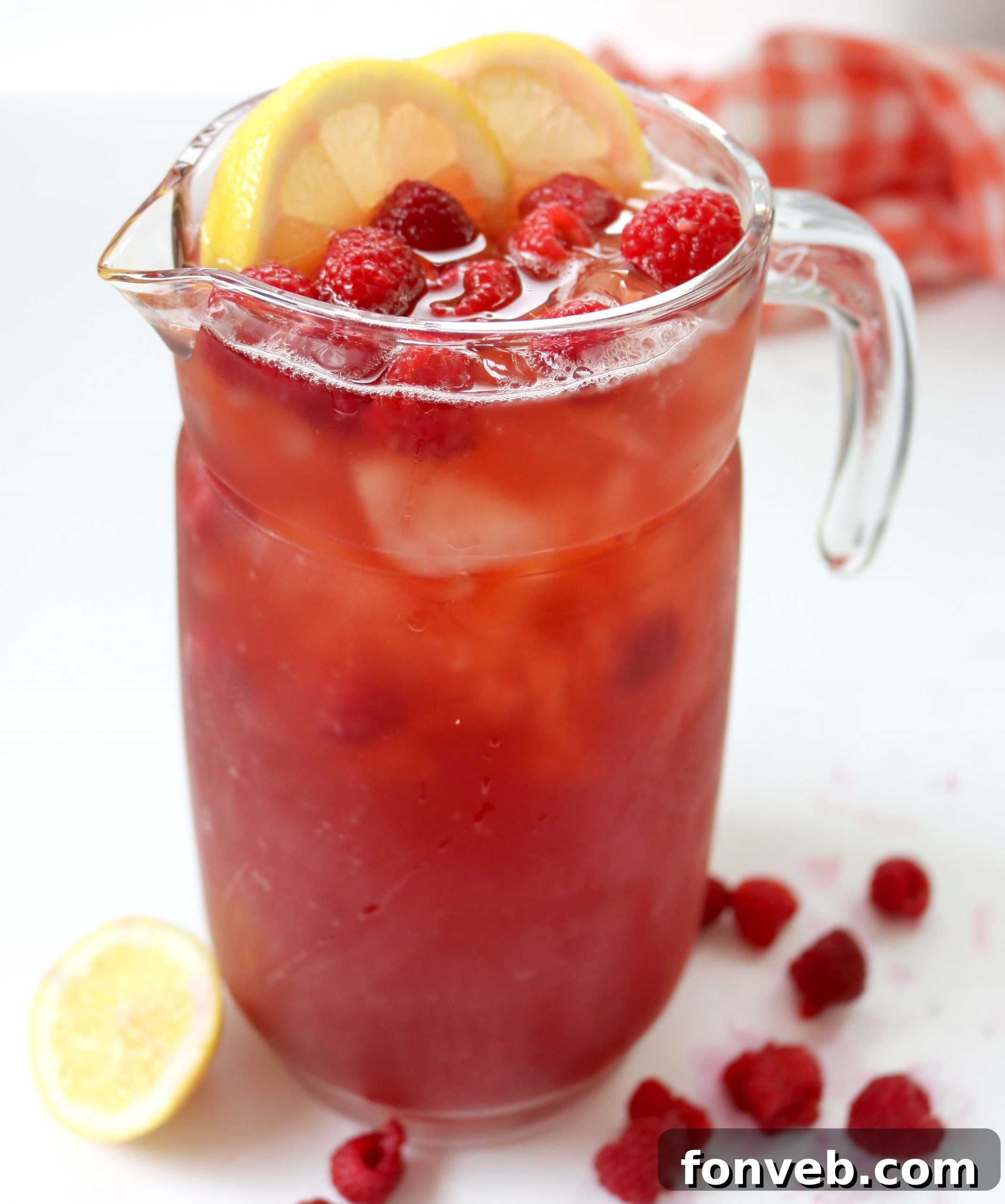 Southern Charm Raspberry Sweet Tea 2 A tall glass of vibrant pink Raspberry Southern Sweet Tea, garnished with fresh raspberries and a sprig of mint, with a pitcher in the background.