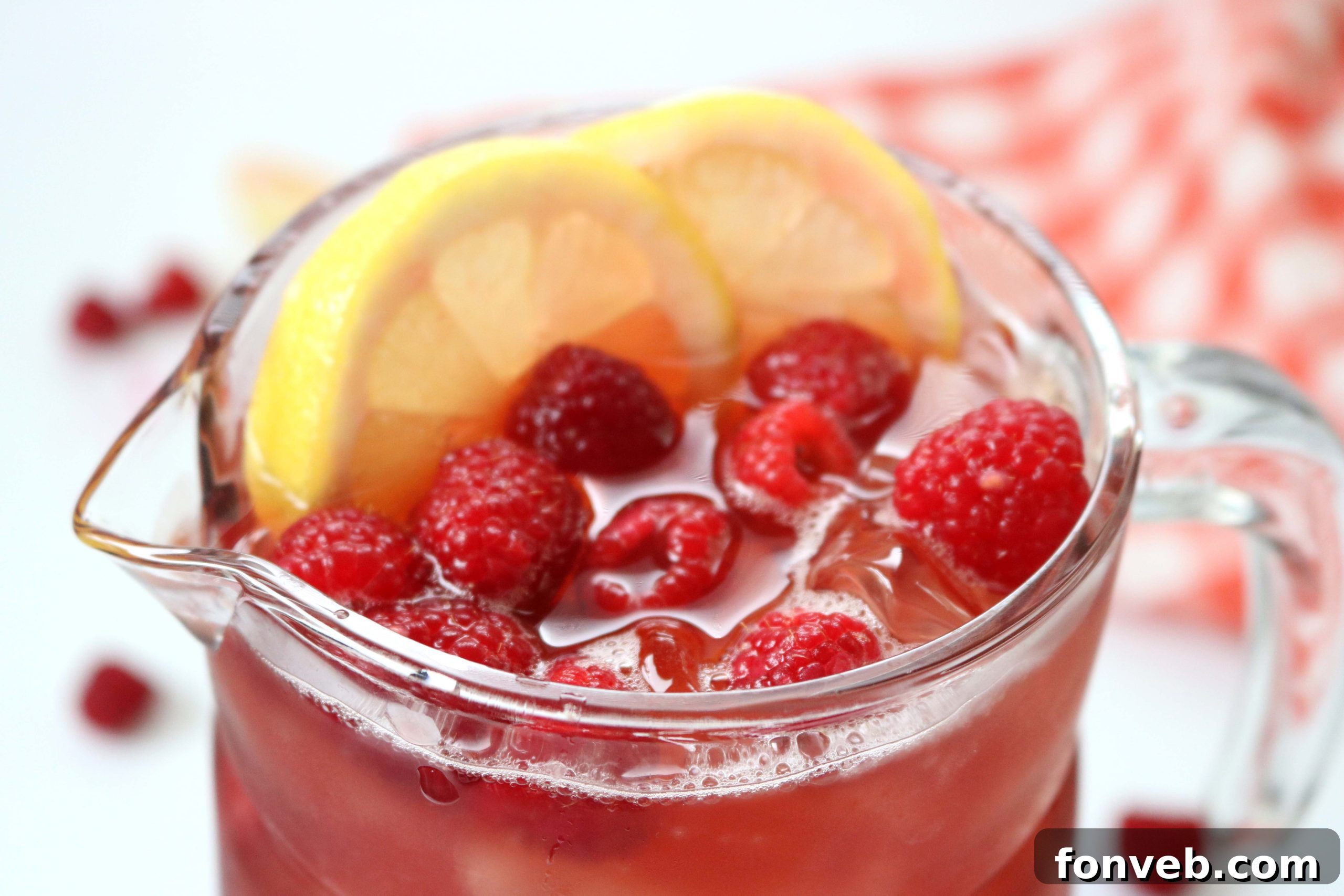 Southern Charm Raspberry Sweet Tea 5 A glass of Raspberry Sweet Tea on a rustic wooden surface, with a pitcher and bowl of fresh raspberries in the background, highlighting its natural beauty and inviting presentation.