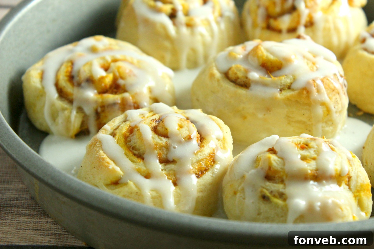 Hand reaching for a perfectly frosted pumpkin cinnamon roll, highlighting the thick icing.
