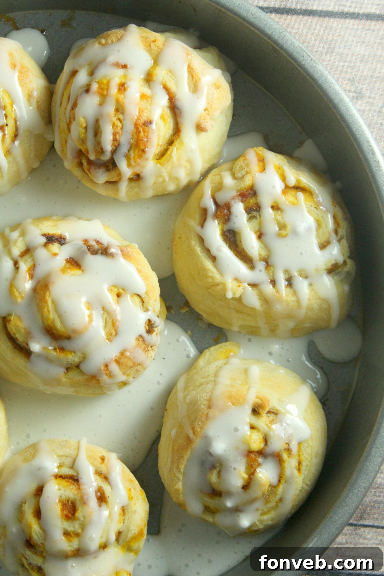 Multiple pumpkin cinnamon rolls with melted frosting, indicating they are served warm and fresh.