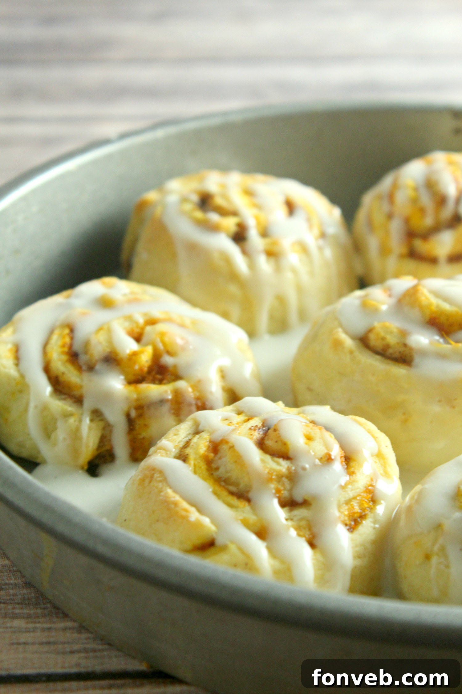 A close-up of pumpkin cinnamon rolls covered in a thick layer of white cream cheese frosting.